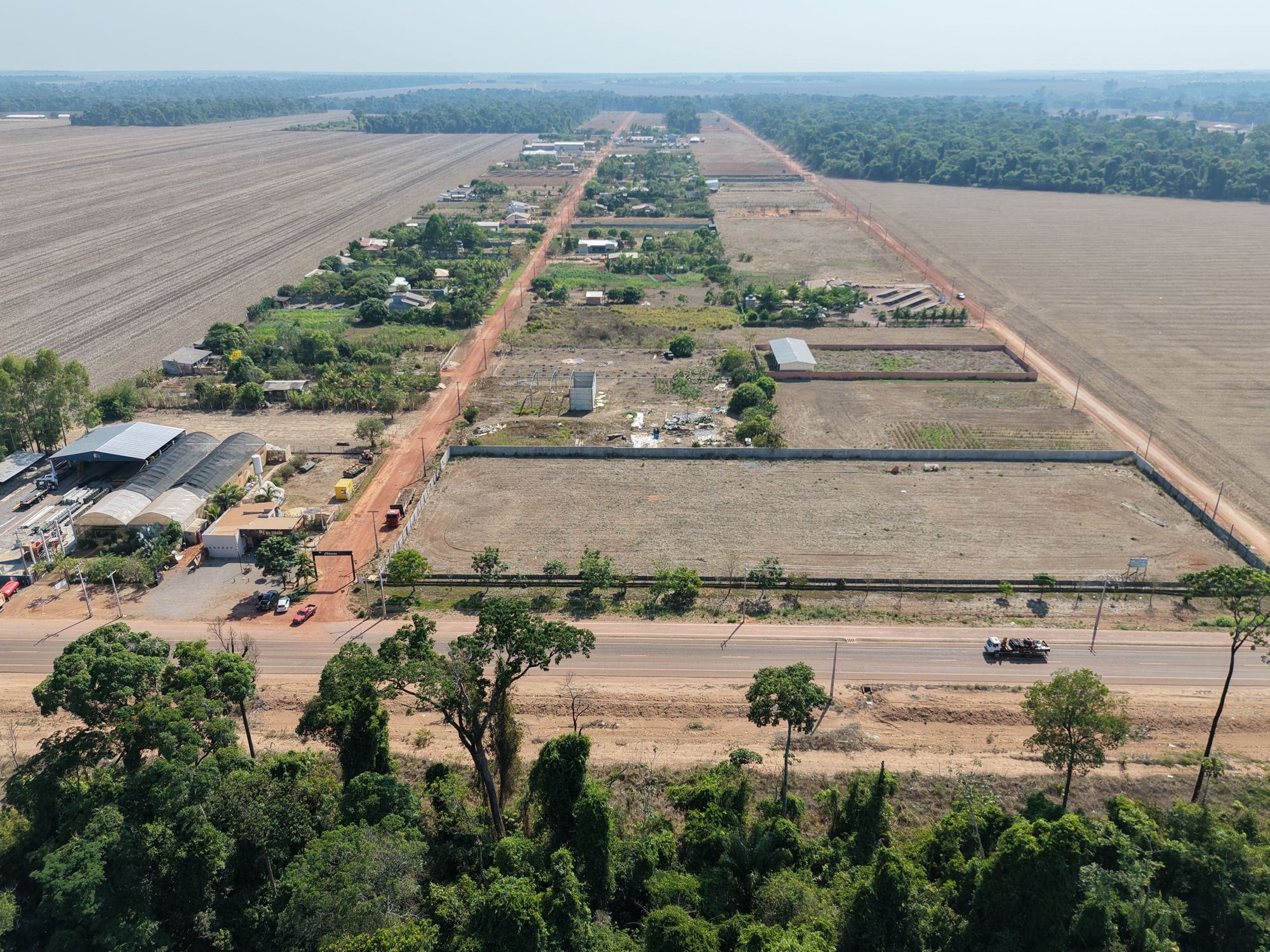 Vista aérea da estrada asfaltada com mata nativa à direita e os lotes ao fundo